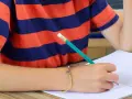 Dziecko w koszulce w paski pisze ołówkiem. Trudności w pisaniu mogą wskazywać na dysgrafię, diagnoza jest ważna.