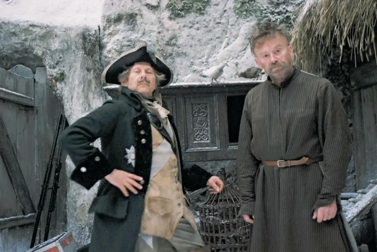 Dwóch mężczyzn w historycznych strojach, jeden w mundurze z epoki, drugi w prostej tunice. Scena jak z filmów do matury, zimowa sceneria.