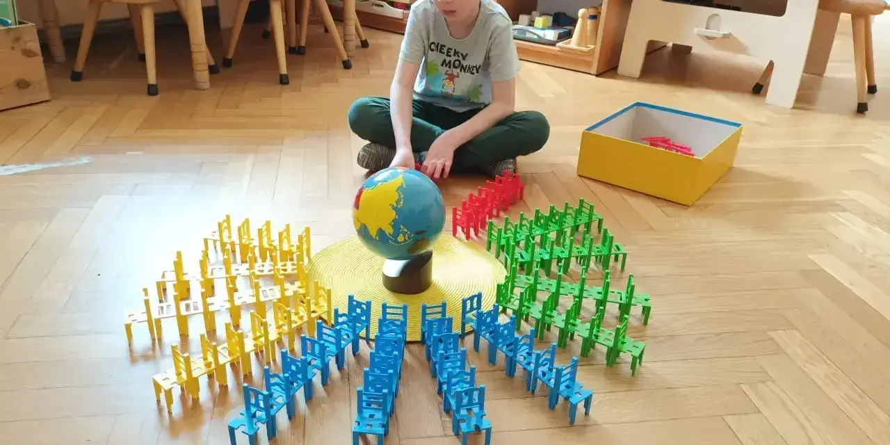 Chłopiec bawi się klockami-krzesłami wokół globusa, ucząc się przez zabawę. To przykład metody Montessori na czym polega nauka przez doświadczenie.