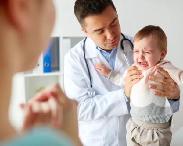 Lekarz uspokaja płaczące dziecko, które przechodzi skok rozwojowy 4 latka. Mama wspiera malucha.