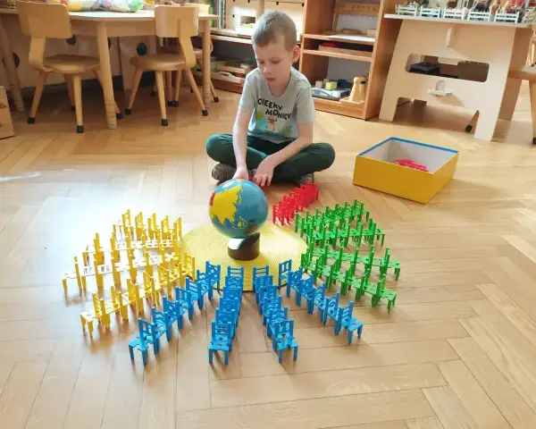 Chłopiec bawi się klockami-krzesłami wokół globusa, ucząc się przez zabawę. To przykład metody Montessori na czym polega nauka przez doświadczenie.