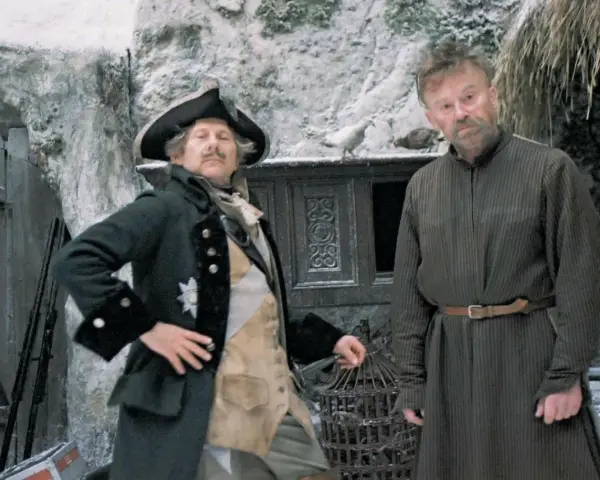 Dwóch mężczyzn w historycznych strojach, jeden w mundurze z epoki, drugi w prostej tunice. Scena jak z filmów do matury, zimowa sceneria.