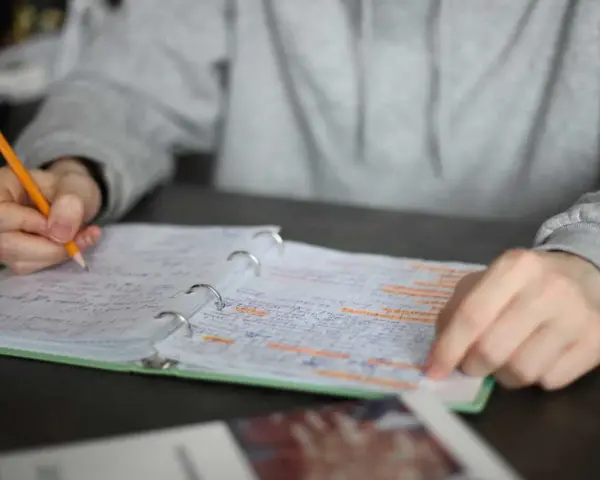 Uczeń pisze w zeszycie, przygotowując się do sprawdzianu. Zeszyt zawiera notatki, które mogą być oceniane według procentowej skali ocen w szkole podstawowej 4-8.