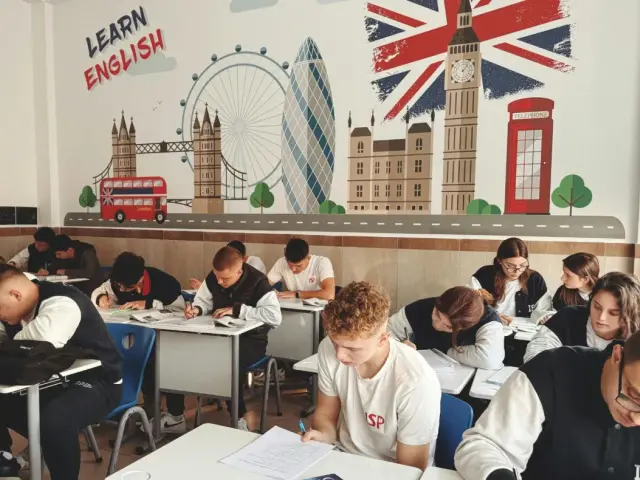 Uczniowie piszą test w klasie z muralem Londynu i hasłem "Learn English".