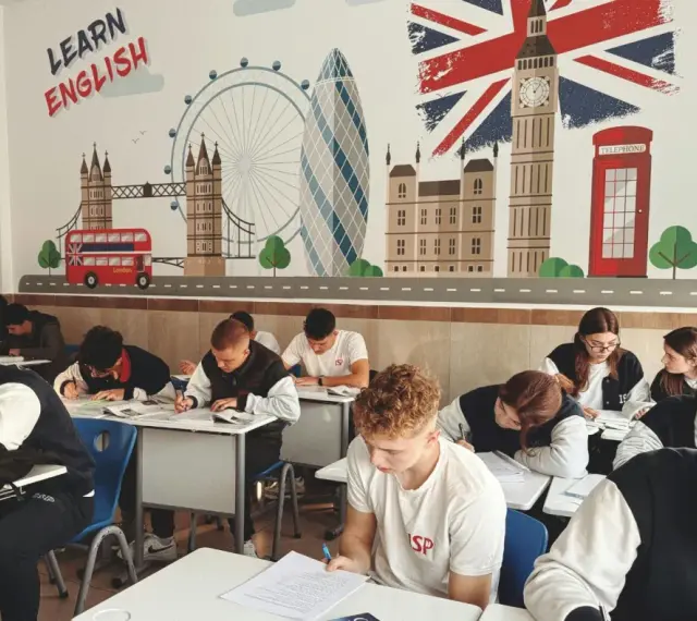 Uczniowie piszą test w klasie z muralem Londynu i hasłem "Learn English".