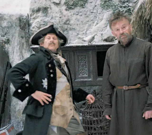 Dwóch mężczyzn w historycznych strojach, jeden w mundurze z epoki, drugi w prostej tunice. Scena jak z filmów do matury, zimowa sceneria.