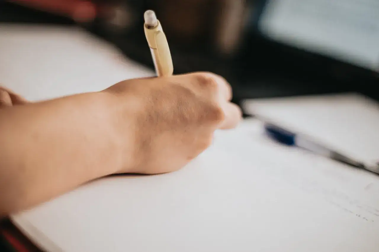 Dłoń pisze długopisem na kartce. Czy matura ustna liczy się na studia? Ważne przygotowanie do egzaminów.