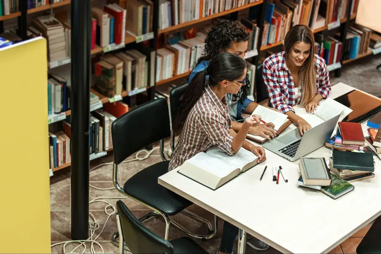 Trzy studentki uczą się w bibliotece. Zastanawiają się, jakie studia po maturze z fizyki i matematyki wybrać.