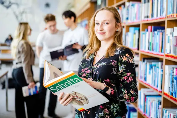 Studentka na Uniwersytecie Wrocławskim, kierunek prawo, przegląda atlas anatomii. W tle inni studenci i regały z książkami.