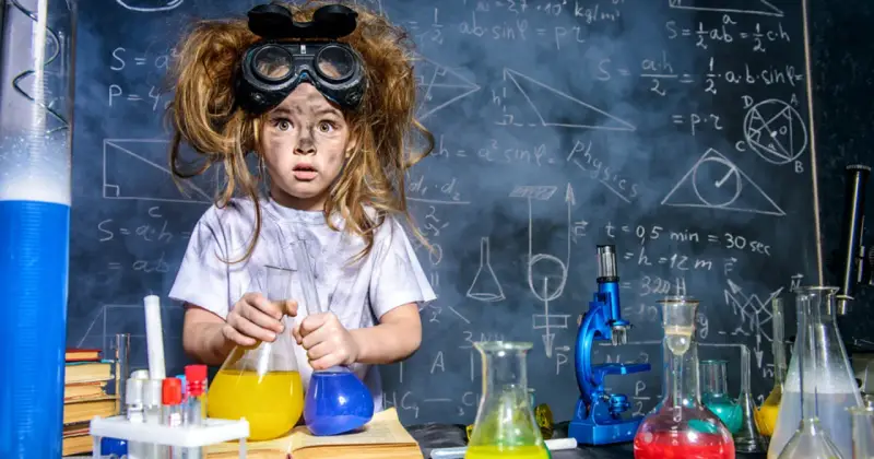 Mała chemik z rozczochranymi włosami i okularami ochronnymi, trzymająca kolby z kolorowymi płynami. W tle tablica z wzorami, idealna do eksperymentów chemicznych dla dzieci.